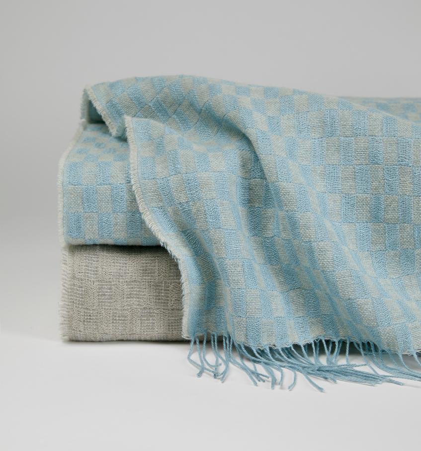 Stack image of the basketweave Palmilla throw in blue and grey against a grey background.