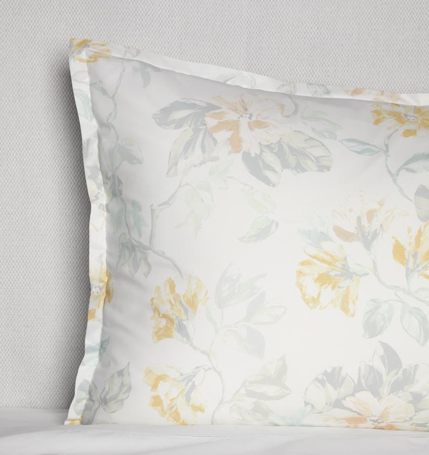 Corner shot of a white cotton sham with a light yellow floral motif against a white background.