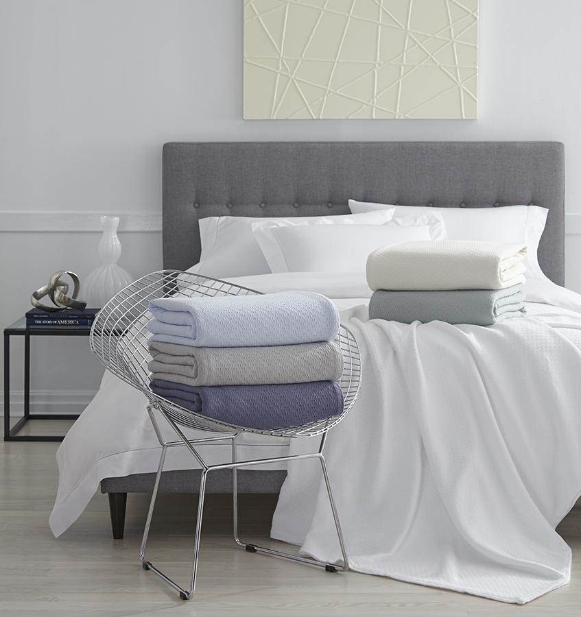 The SFERRA Corino lightweight, breathable cotton blanket in white, ivory, seagreen, and powder blue.